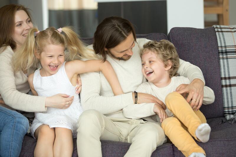 Foreldre og barn sitter i sofa og leker og ler